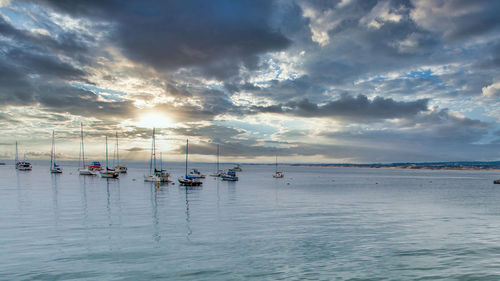 Sailboats moored in sea against sky during sunset