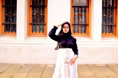 Portrait of young woman standing against building