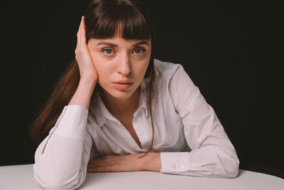 Portrait of woman sitting against black background