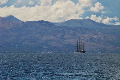 Sailboat sailing on sea by mountains against sky