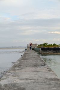 Rear view of people standing on shore against sky