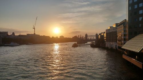 Scenic view of river by buildings against sky during sunset