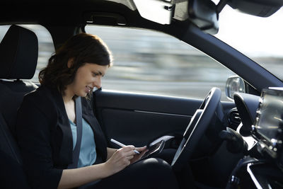 Smiling businesswoman using tablet pc in autonomous driving car