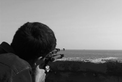 Man aiming sea against clear sky