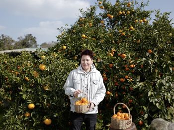 Portrait of smiling man holding oranges in basket at farm
