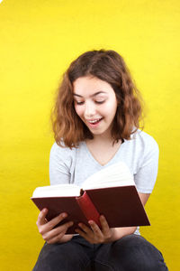 Beautiful young woman reading book against yellow wall