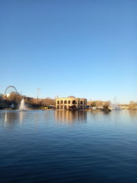 Buildings by lake against clear blue sky