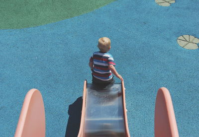 Rear view of boy playing on slide at playground