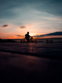 Silhouette man sitting on shore against sky during sunset