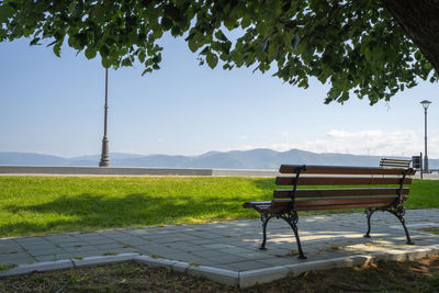 Empty bench on field against sky