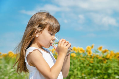 Side view of young woman drinking water while standing against sky