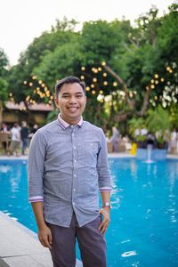 Portrait of young man standing by swimming pool