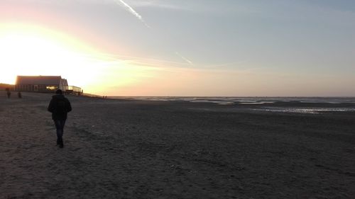 Rear view of silhouette man walking on beach at sunset