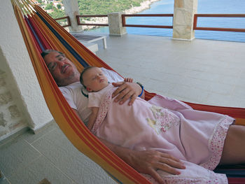 Portrait of smiling father holding daughter while relaxing on hammock