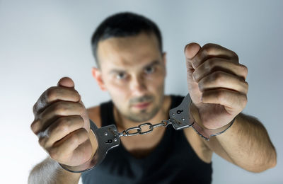 Portrait of man with handcuffs against gray background