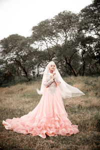 Bride wearing wedding dress standing against trees in forest