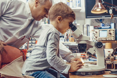 Science teacher and small boy analyzing circuit board under a microscope in it laboratory.