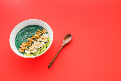 A spirulina smoothie bowl with banana, walnuts, kiwi and chia seeds on red background