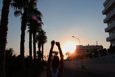 Silhouette woman on street in city against sky during sunset