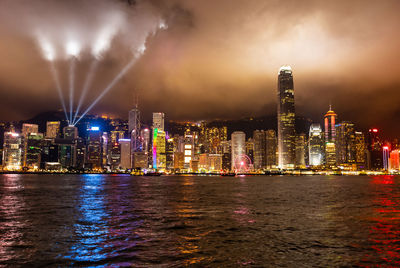 Illuminated buildings by river against sky at night