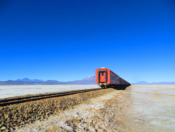 View of red train in desert against clear blue sky