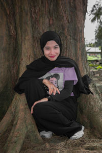 Portrait of smiling woman sitting on tree trunk