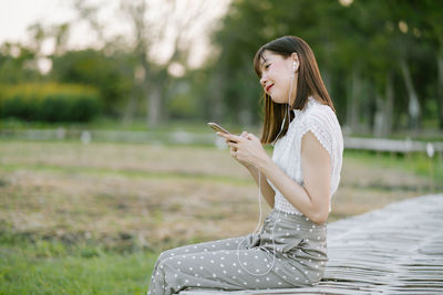 Side view of young woman using mobile phone outdoors