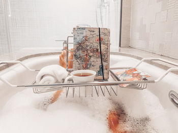 Low section of woman with drink and map bathing in bathtub