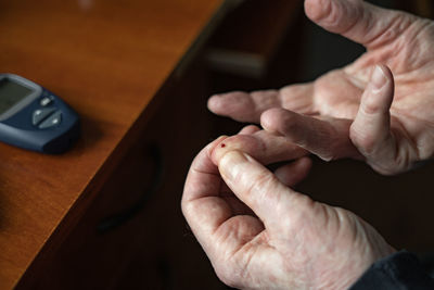 From above of crop unrecognizable person with pierced finger sitting at table with glucose meter for making blood sugar test person