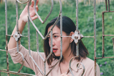 Portrait of young woman holding camera while standing by fence