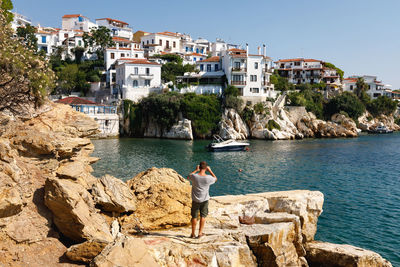 Man standing on rock by sea against sky