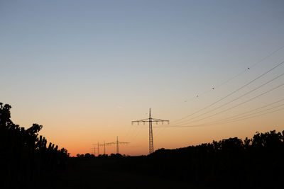 Silhouette electricity pylons against clear sky during sunset