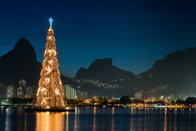 Illuminated artificial christmas tree in city against sky at night