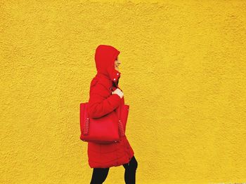 Woman in profile with red hood walks in front of a yellow wall