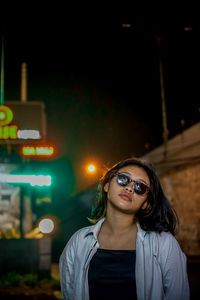 Portrait of young woman standing against illuminated street at night