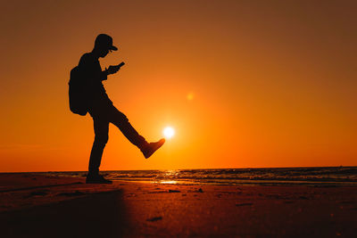 Silhouette man standing on beach against sky during sunset