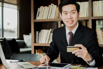 Portrait of businessman using digital tablet while holding credit card at desk