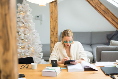 Businesswoman using digital tablet at home by christmas tree