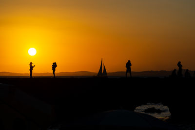 People, in silhouette, are seen on the porto da barra pier enjoying the sunset