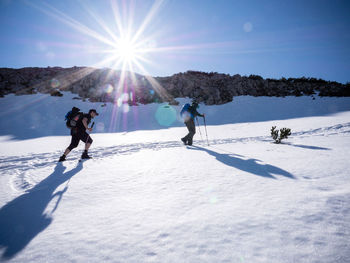 People skiing on snow covered landscape against sky