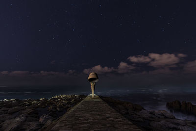 Rear view of woman standing by sea against sky at night