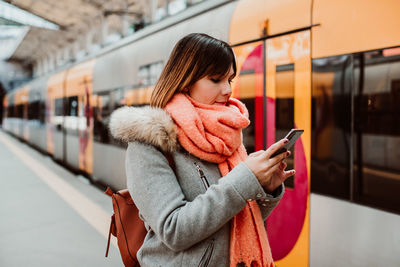 Woman using mobile phone while standing at railroad station platform