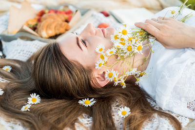 High angle view of woman holing flowers lying on bed with food