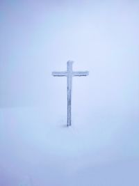 Cross on snow covered field against sky