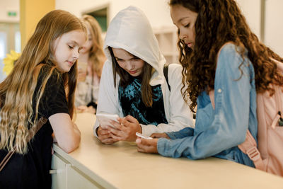 Female students using phone while standing in school corridor during lunch break