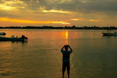 Silhouette of a man standing taking photos with a mobile phone at sunset at shela beach, lamu, kenya