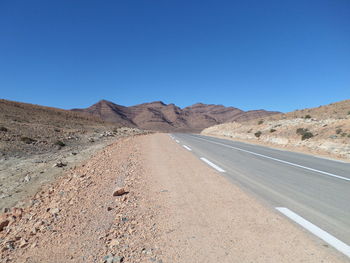 Road leading towards mountains against clear blue sky