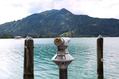 Hand-held telescope by sea against mountain