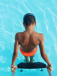 High angle view of shirtless boy standing on ladder in swimming pool