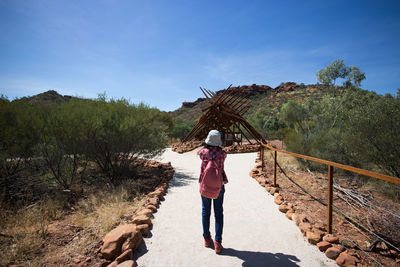 Rear view of woman walking on footpath at mountain against sky